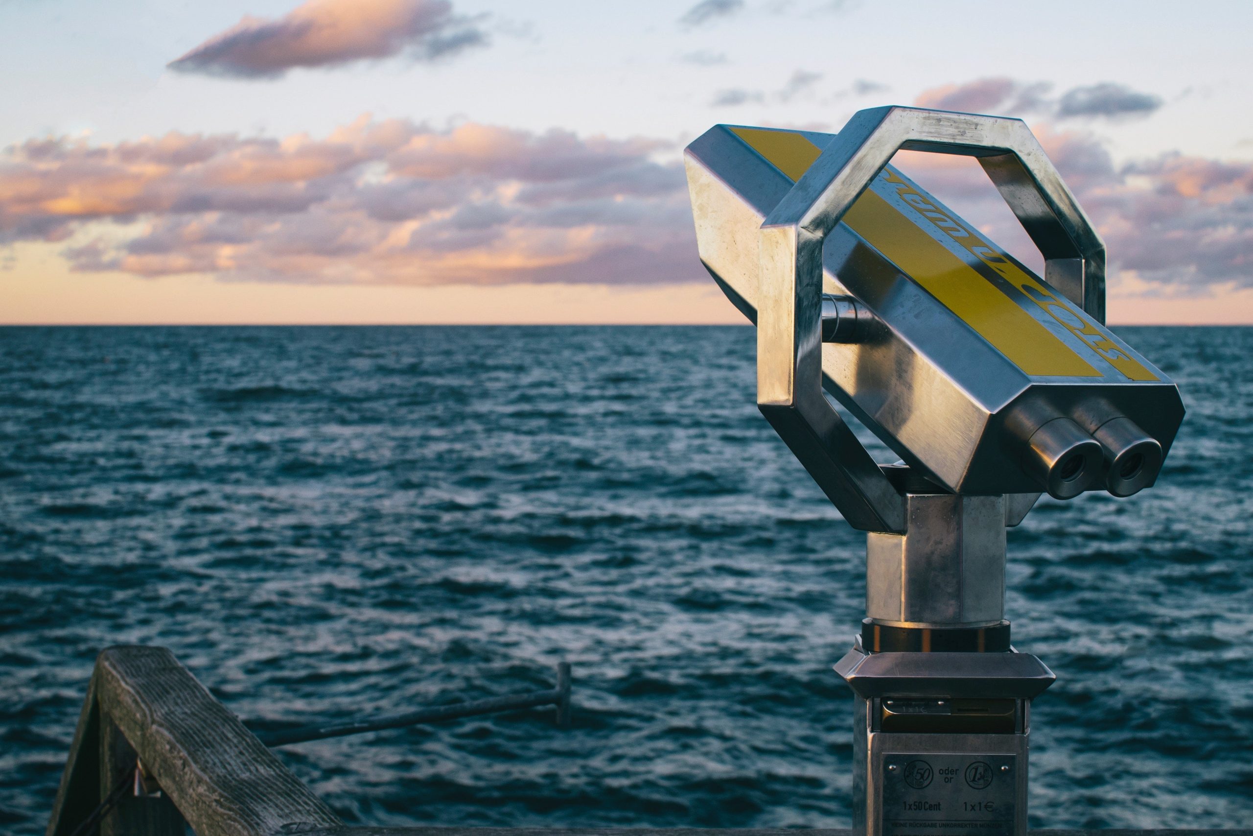 Tower viewer overlooking a vast ocean under a sky filled with pink and orange clouds at sunset. The scene conveys calm and contemplation.