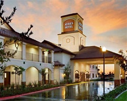 Hotel exterior at sunset with a prominent tower featuring a sign, arched windows, and a reflective water feature, creating a warm, inviting ambiance.