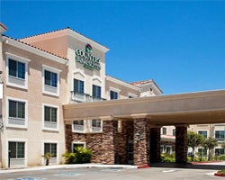 A beige, three-story hotel under a clear blue sky, features large windows and a stone-accented entrance, conveying a welcoming, upscale atmosphere.