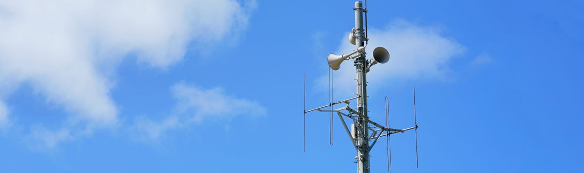 A tall telecommunications tower stands against a vibrant blue sky with scattered white clouds. The scene conveys a sense of modern connectivity.