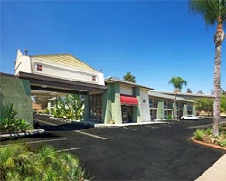 Exterior of a motel on a sunny day, featuring a drive-through entrance, palm trees, and a well-maintained parking lot, conveying a welcoming atmosphere.