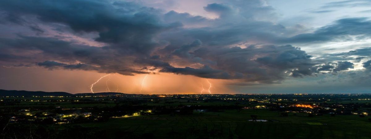 A dramatic landscape of a stormy sky with vivid lightning strikes over a dark, sprawling cityscape at dusk, with an ominous and powerful atmosphere.
