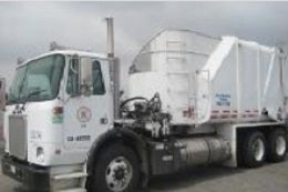 A white garbage truck with city logos and identification numbers is parked on a cloudy day. The truck is large and industrial, conveying utility and functionality.