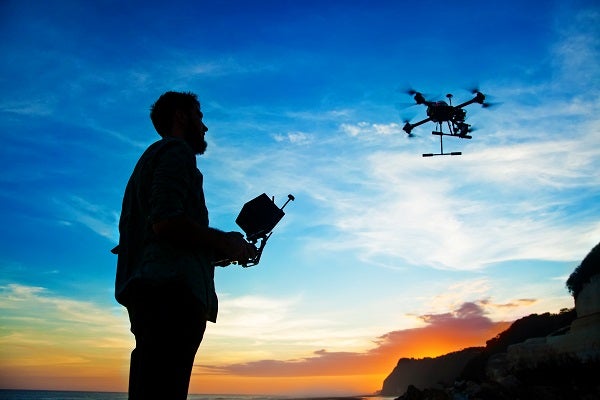 Silhouette of a person controlling a drone at sunset, with a vivid blue and orange sky, creating a serene and adventurous atmosphere.