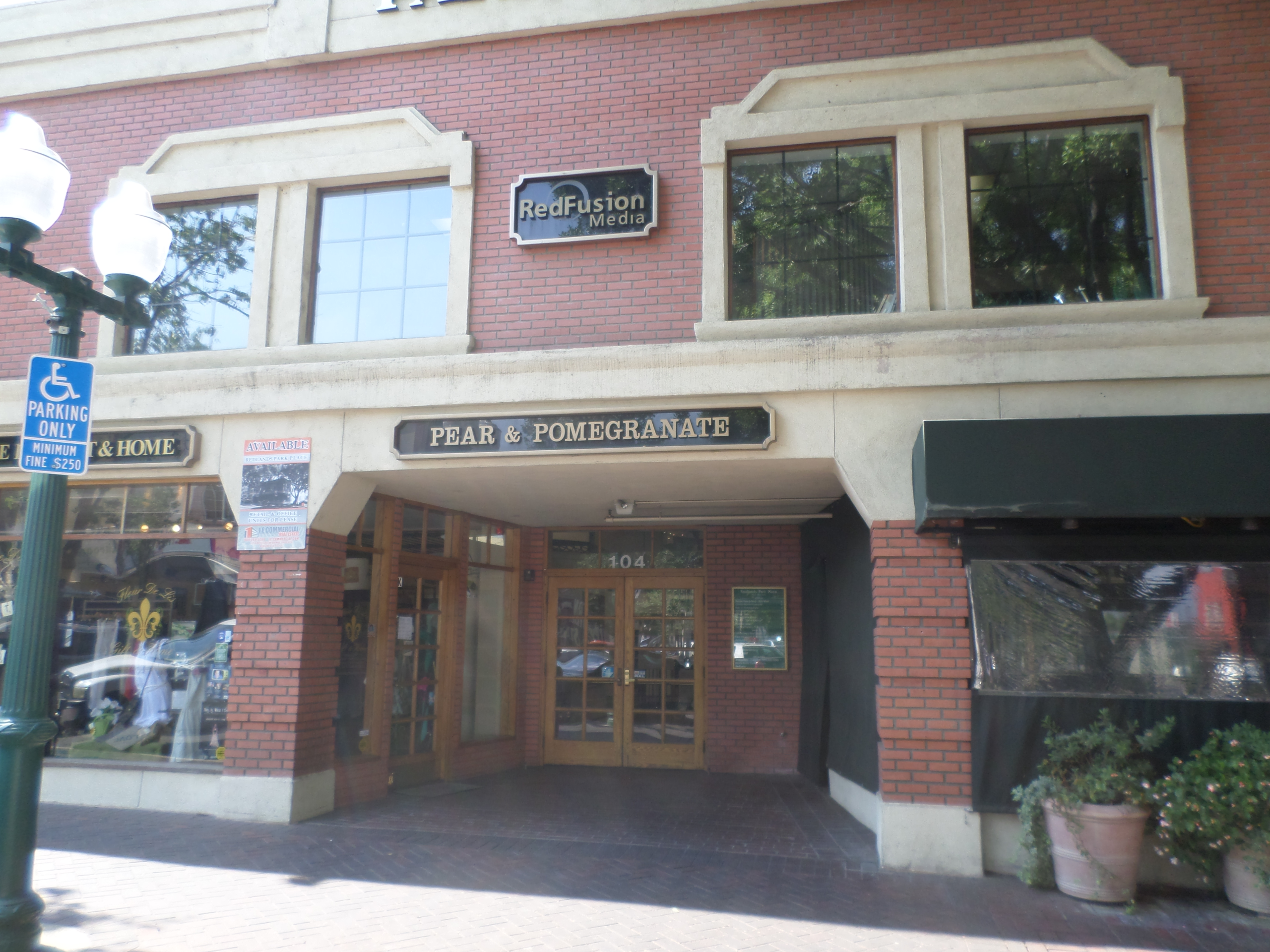 Street view of a brick building with "Pear & Pomegranate" and "RedFusion Media" signs. A handicapped parking sign is visible, creating a welcoming atmosphere.