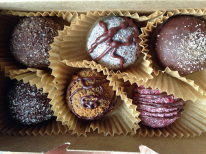 Box of six assorted truffles in paper cups, topped with chocolate drizzle and sugar dusting, conveying delicacy and indulgence.
