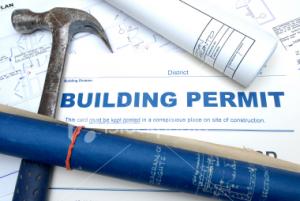 A hammer and rolled blueprints lie on a building permit document, conveying construction and planning. The tone is professional and focused.