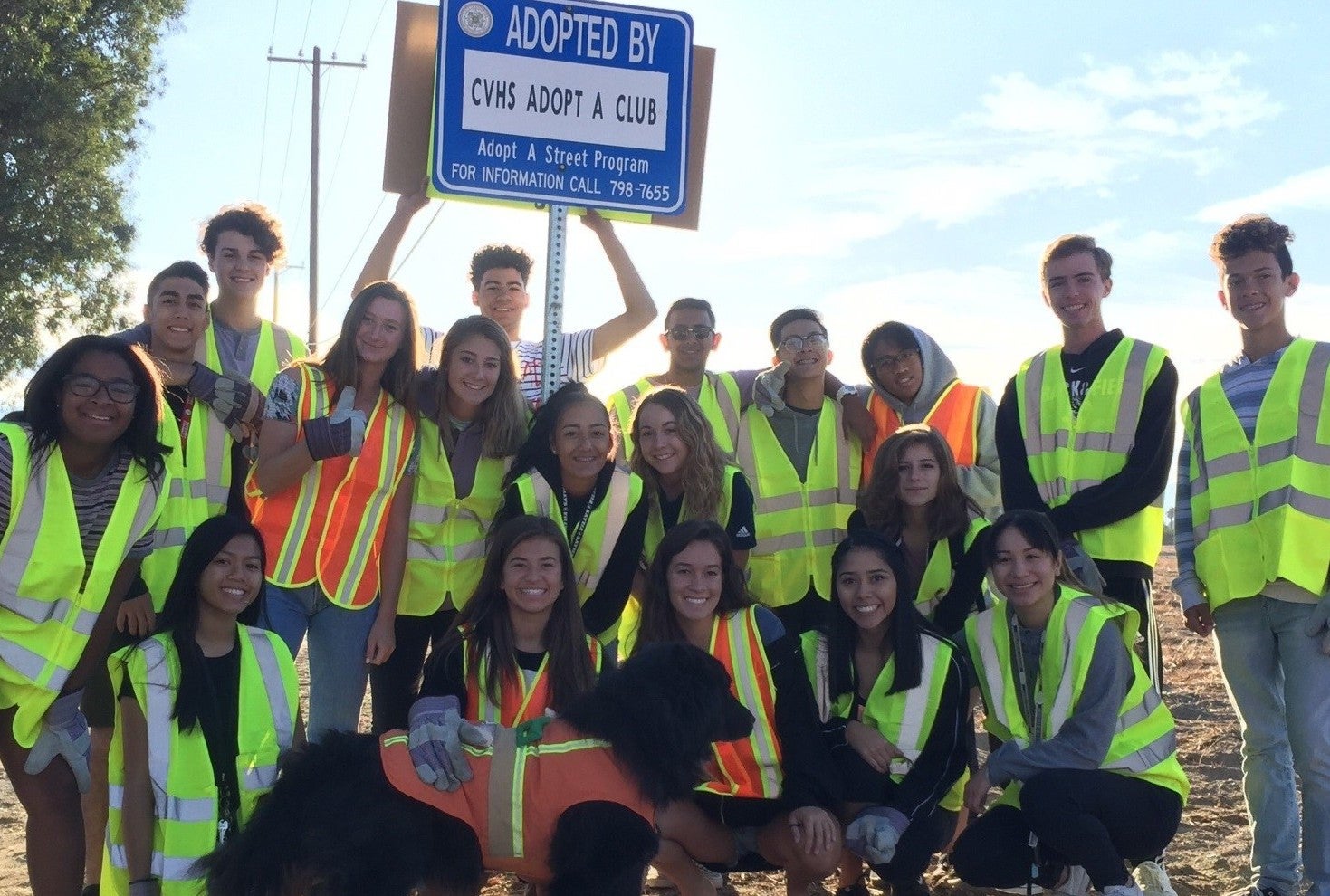 Children in safety vests next to adopt a street sign