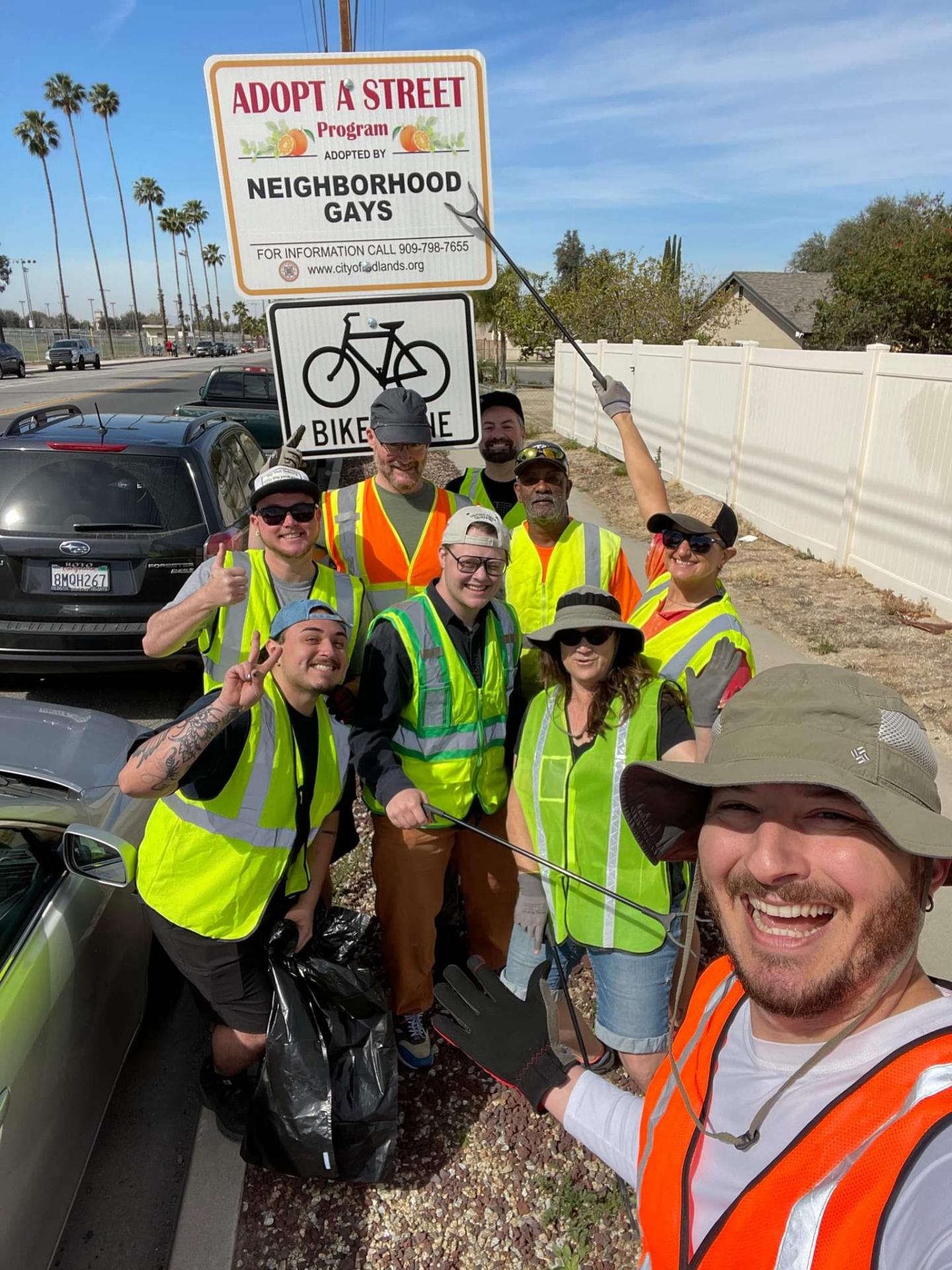 Group of people in safety vests stand next to adopt a street sign