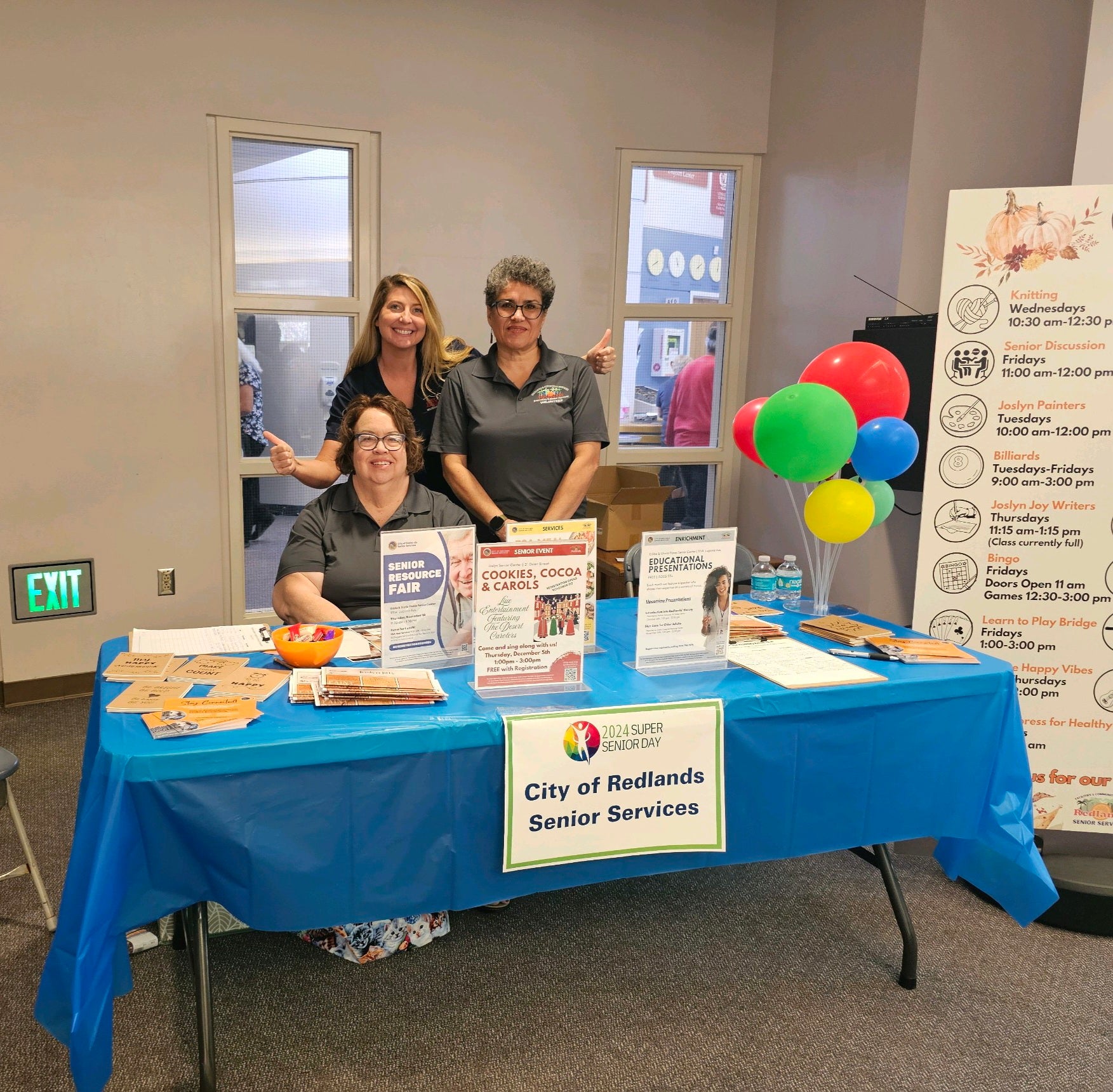 Three smiling individuals stand behind a table with informational brochures, a 