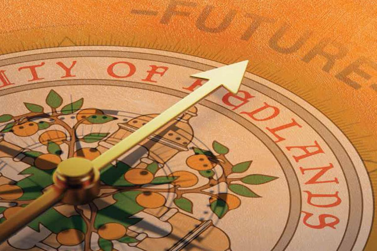 A close-up of a compass with its needle pointing toward the word "FUTURE" in the background, partially overlaid on the University of Redlands emblem.