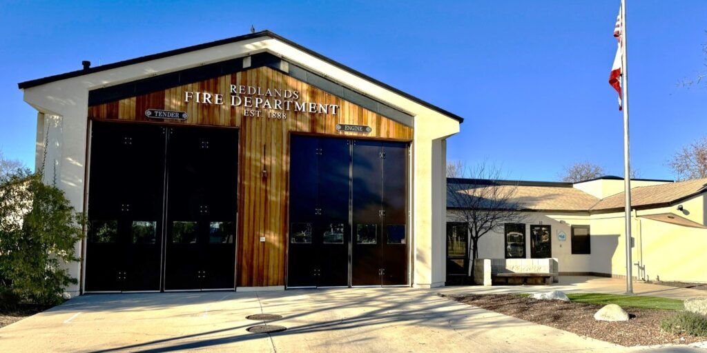 Redlands fire station 263 building marked "Redlands Fire Department" with two large garage doors and a flagpole with the California state flag outside.