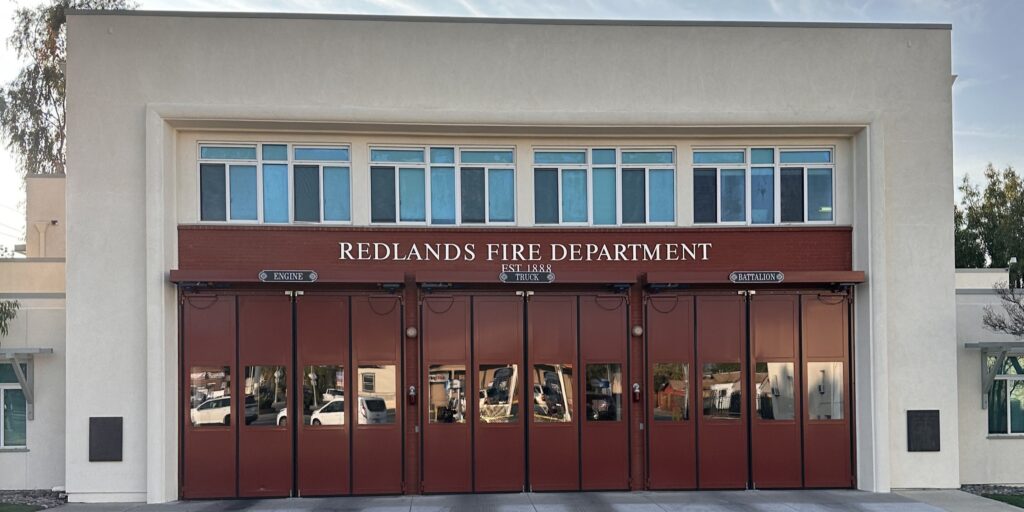 Front view of the Redlands Fire Downtown Station 261 building with six closed red bay doors and signage above the entrance.