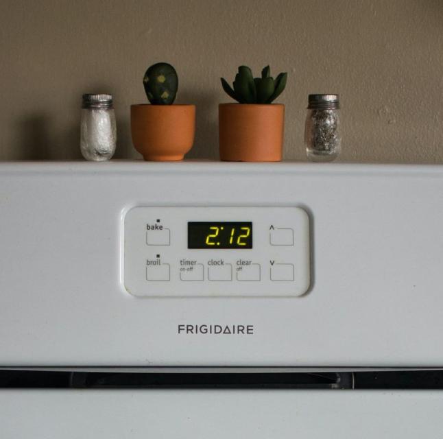 A Frigidaire oven with a digital clock reading 2:12, topped with two small potted succulents and two spice shakers.