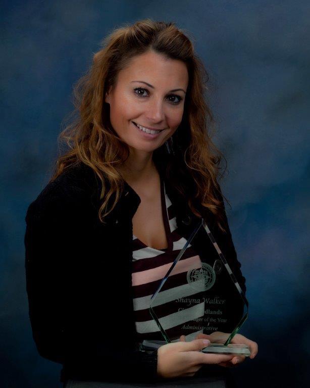 Woman with long brown hair holds a glass award and smiles at the camera against a blue studio backdrop.