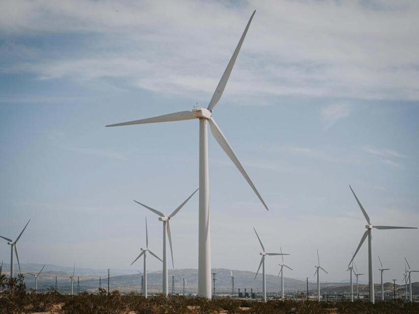 Multiple wind turbines are spread across a dry landscape under a partly cloudy sky, generating renewable energy.