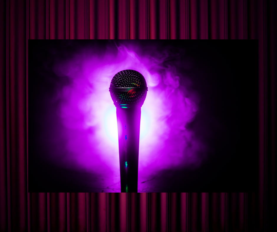 A microphone stands upright in front of a dark background with purple light and smoke behind it.
