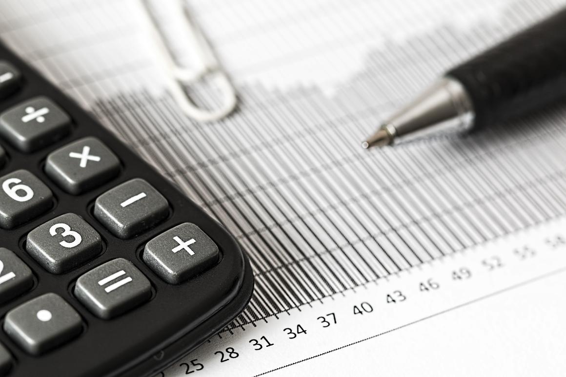 Close-up of a calculator, pen, and paperclip on a printed financial chart with bar graphs and numerical data.