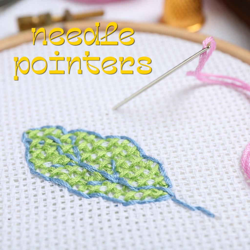 An embroidery hoop with a stitched green leaf, a threaded needle, and the words “needle pointers” in yellow text on white fabric.